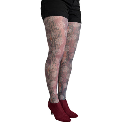 A person wearing sheer patterned tights with a floral and script design in muted pink, beige, and gray tones, paired with black shorts and burgundy ankle boots, shown against a plain white background.